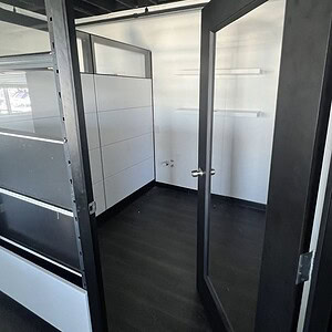 Modern office pod with glass door, tiled floor, and white interior panels.