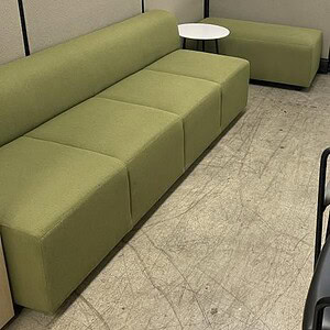 Green modular lounge sofa with small white side table in office space.