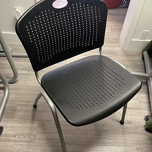 Black stacking chair with perforated backrest and seat, ideal for cafes and guest seating. Durable,.