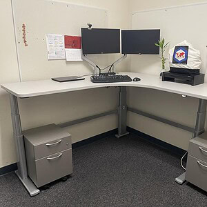 Adjustable desk with dual monitors and storage drawers.