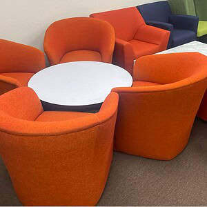 Orange lounge chairs surrounding a white round table, mid-century modern style, ideal for office or.