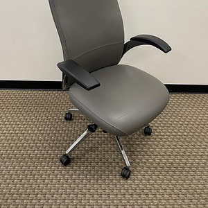 Grey ergonomic leather office chair with adjustable armrests and rolling casters.