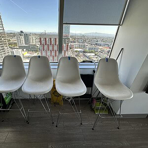 Modern white Eames-style bar height stools in a high-rise office setting.