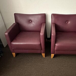 Two burgundy leather armchairs with wooden legs in a modern office setting.