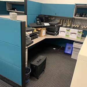 Office cubicle with blue fabric panels and organized workspace setup.