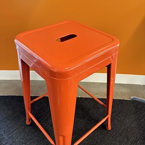 Bright orange metal stackable bar stool for modern kitchen or bar decor. Durable, stylish, and space.