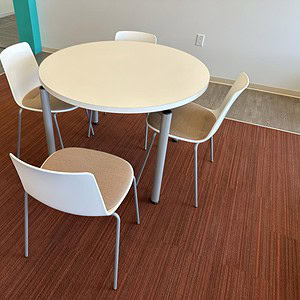 White and brown stack chairs around a round table in a modern office setting.