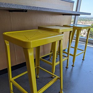 Bright yellow square bar height stool with metal frame and footrest.