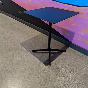 Square black metal table with a sturdy base, ideal for modern interior and outdoor spaces.