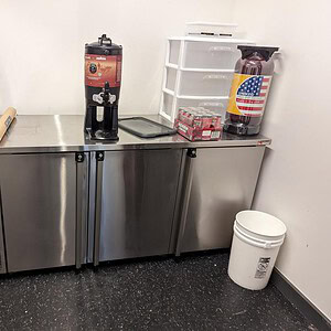 Refrigerator credenza with stainless steel finish and storage for beverages and supplies.