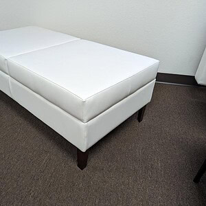 White leather upholstered bench with dark wooden legs, modern office furniture.