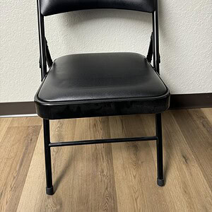 Black folding chair with metal base and vinyl seat, ideal for events and seating solutions.