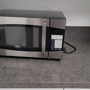 Oster commercial microwave oven in sleek silver finish for commercial kitchen use.