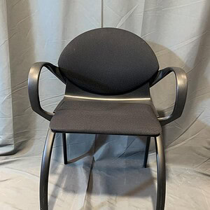 Modern Vecta stacking chair with black cushioned seat and armrests.