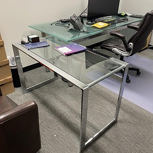 Chrome & glass desk with dual monitors, office chair, and accessories.