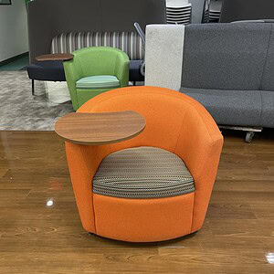 Comfortable orange soft chair with built-in desk for versatile workspace comfort.