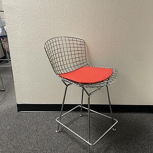Vitra chrome wire chair with mid back and orange cushion, modern office seating.