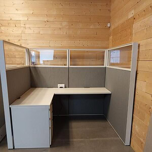 Office cubicle with grey fabric panels and glass partitions, compact workspace setup.