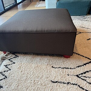 Ottoman square in charcoal fabric with red legs, perfect for modern living room decor.