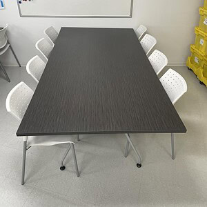 Driftwood surface break room table with white chairs, ideal for office meeting spaces.