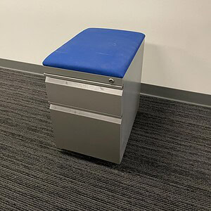 Dark grey mobile pedestal with blue cushion for office storage and organization.