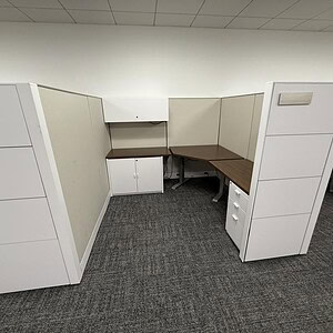 Office cubicles with white panels and brown desks for workspace organization.
