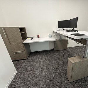 Modern height-adjustable executive desk with dual monitors and storage in office setting.