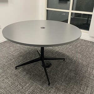 Round grey conference table with a sturdy black base, ideal for modern office meeting rooms and coll.