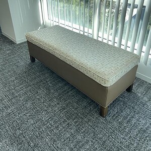 Rectangular plush ottoman in beige with dark wooden legs, ideal for modern living spaces.