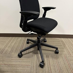 Office chair with black fabric upholstery, ergonomic design, adjustable armrests, and casters for mo.