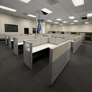 Office cubicles with white and grey panels in a bright, open workspace.
