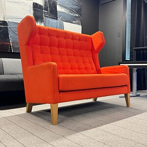 Orange wingback sofa with wooden legs, modern design, perfect for stylish living spaces.