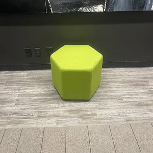 Ottoman with green fabric upholstery, hexagonal shape, modern design.
