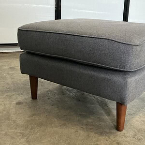 Grey living room ottoman with wooden legs for versatile seating and decor.