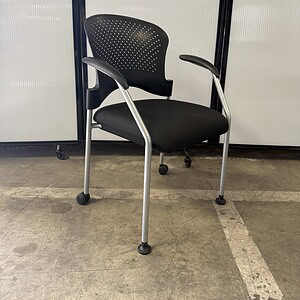 Black training room chair with perforated backrest on casters.