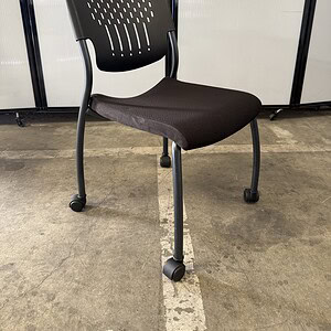 Office chair with armless black fabric seat and perforated backrest, mounted on casters for easy mob.