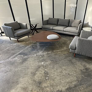 Stylish grey upholstered sofa and armchair set with wooden coffee table in contemporary living room.