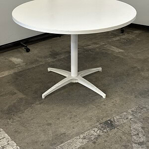White round table with steel base, ideal for office or conference room settings.