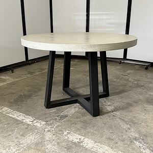 Modern round table with grey plaster top and black metal base, 48" wide.