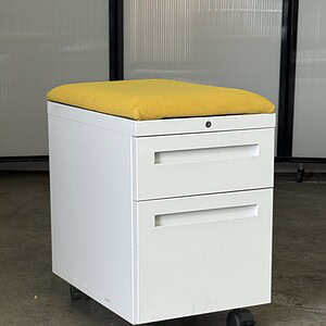 Herman Miller mobile pedestal with removable yellow cushion top, ideal for office storage and comfor.