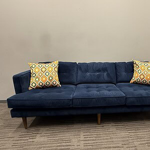 Elegant blue lounge sofa with wooden legs and patterned pillows.