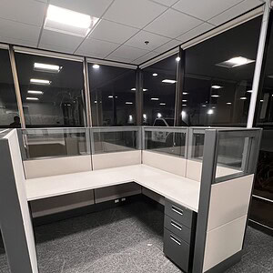 Modern glass office cubicle with white desk and gray drawers, ideal for workspace privacy.