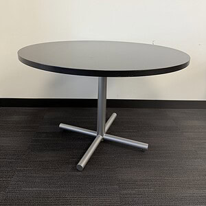 Modern round table with black top and silver base, ideal for office or dining spaces.