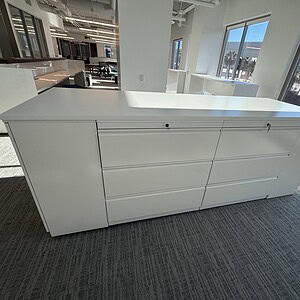 Modern white storage island with three drawers, ideal for kitchens or offices.