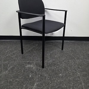 Black stack chair with armrests in a minimalist office setting.