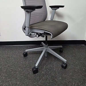Ergonomic Steelcase Think Silver office chair with mesh back and adjustable arms.