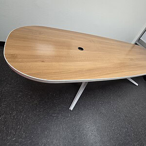 Walnut and white oval conference table with steel legs in modern office setting.