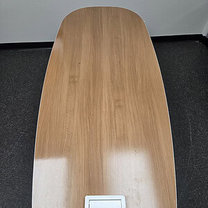 Wooden oval table with power outlet and steel legs for office or conference room.
