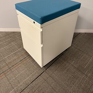 White mobile pedestal with blue cushioned top for office storage.