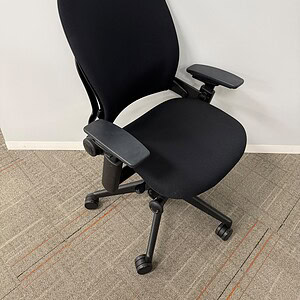 Black ergonomic office chair with adjustable armrests on carpeted floor.